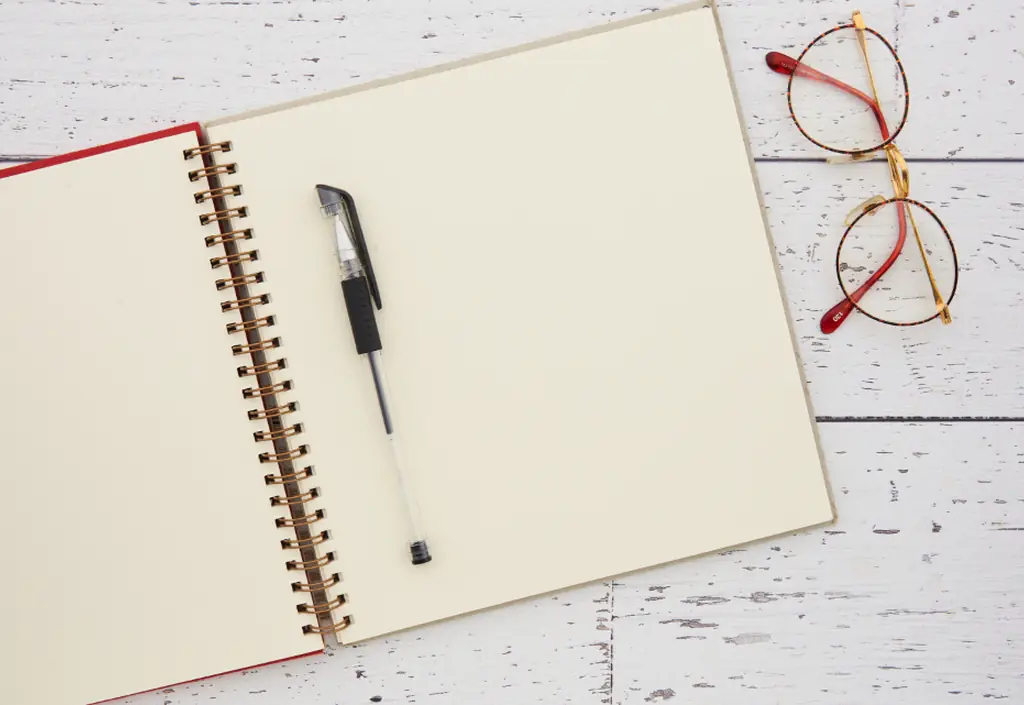 Des lunettes et un stylo posés à côté d’un carnet ouvert, sur une table claire