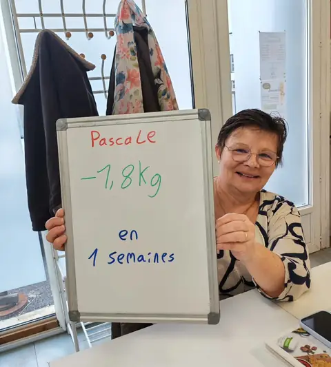 Dans la salle, une membre pose avec son bilan noté sur une ardoise blanche