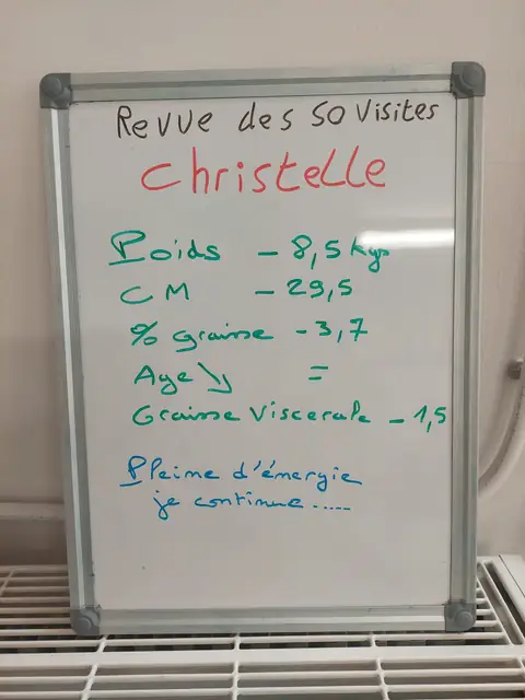 Dans la salle, une membre pose avec son bilan noté sur une ardoise blanche